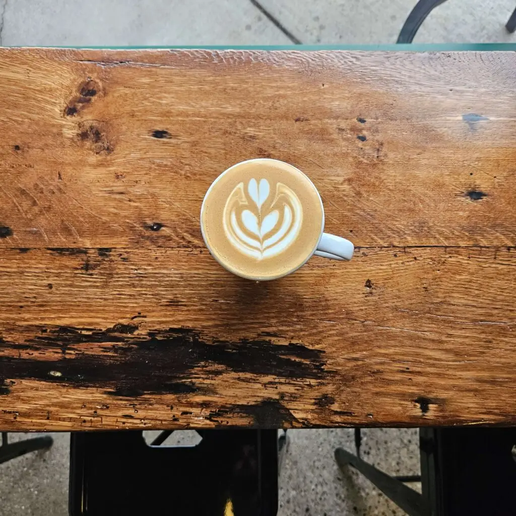 A perfectly crafted cappuccino with intricate latte art, served in a white cup on a rustic wooden table.